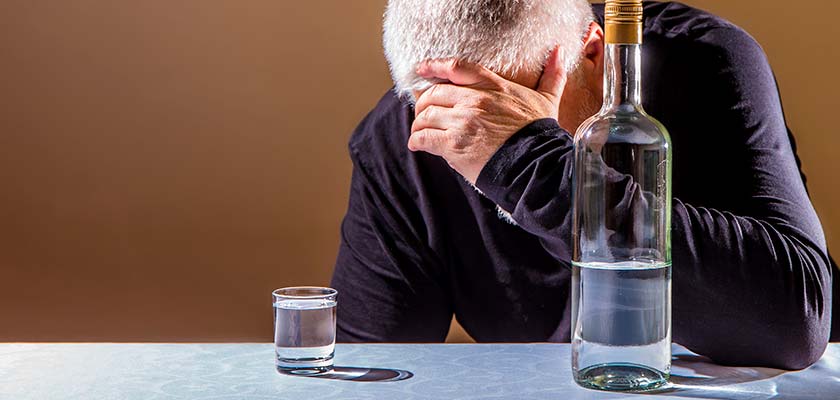 мужчина сидит за столом с бутылкой водки