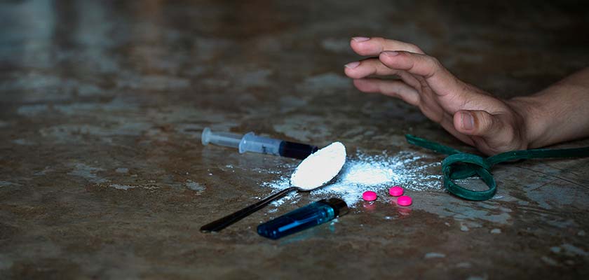 мужчина тянет руку к таблеткам и наркотикам